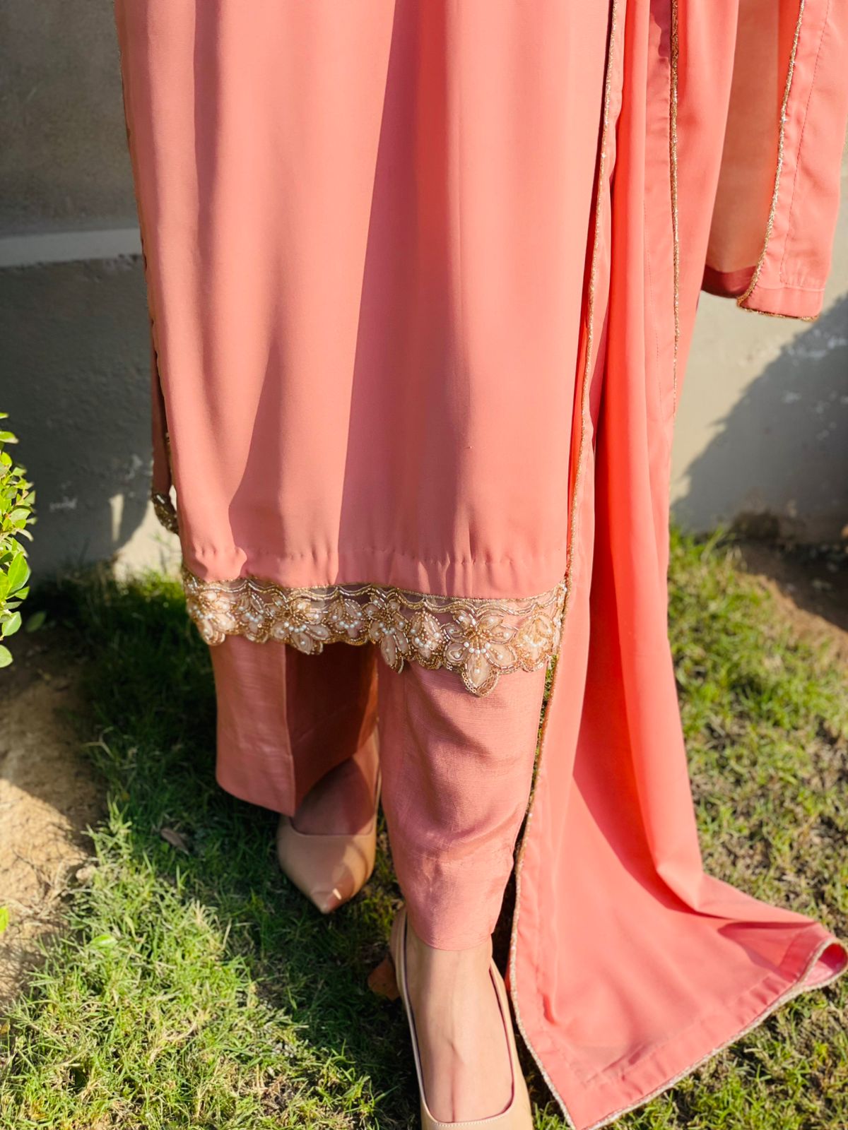 Coral pink traditional outfit with gold embroidery on a grassy ground