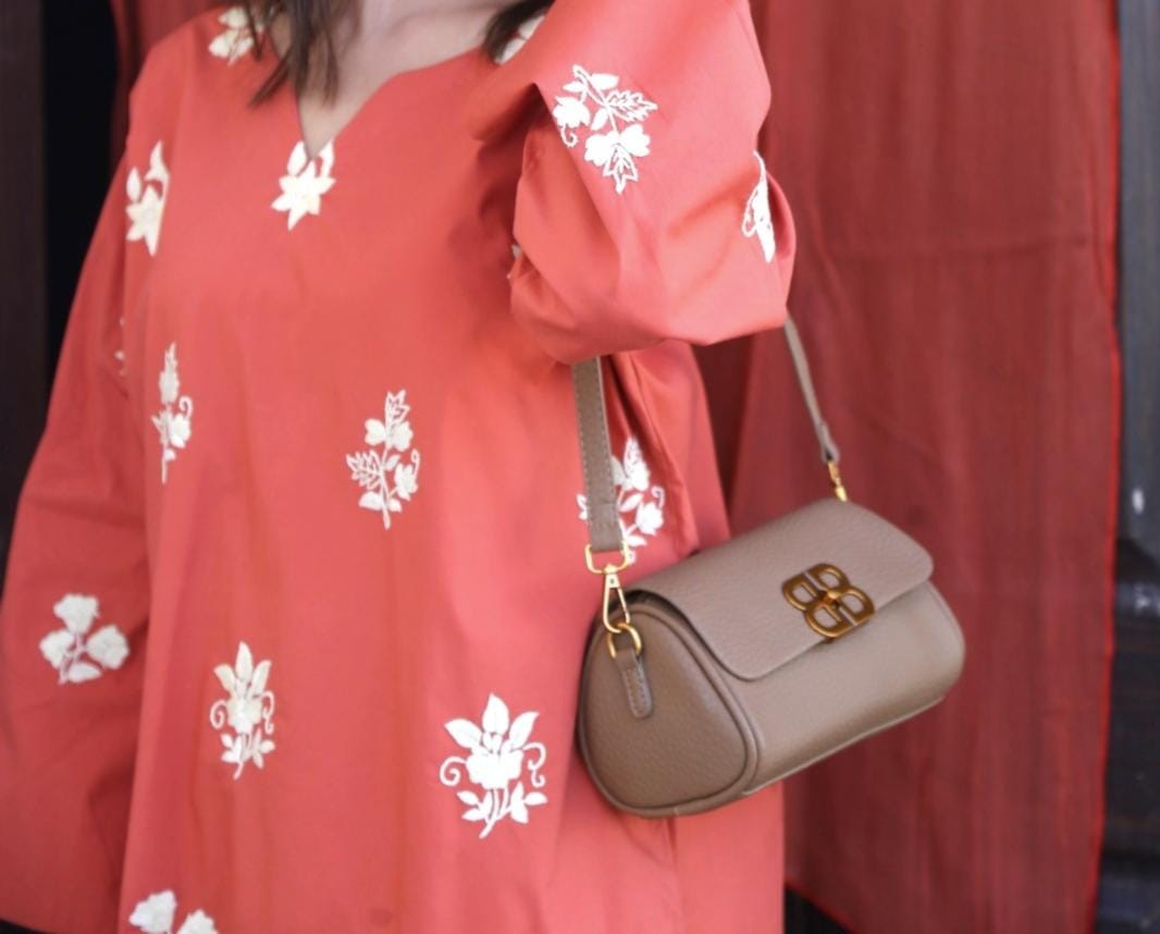Person wearing a red floral dress holding a beige handbag.