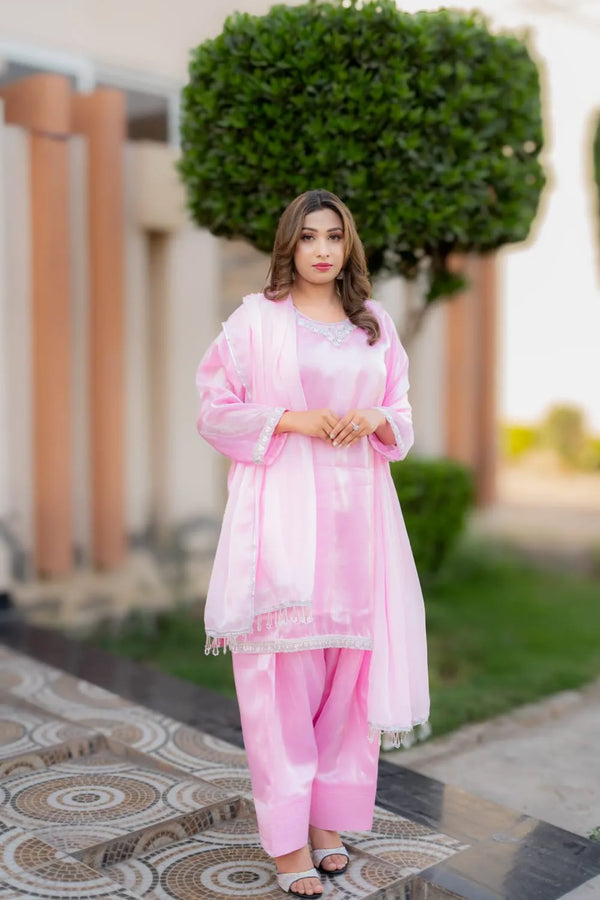 Woman in a pink traditional outfit standing outdoors with greenery in the background