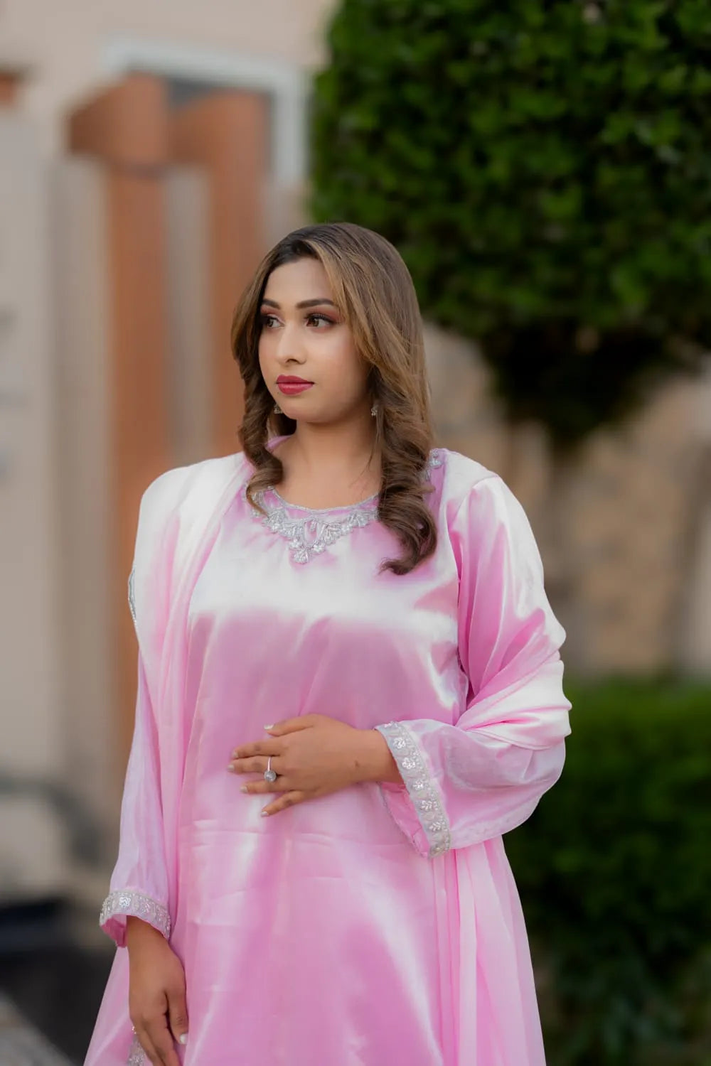 Woman wearing a pink and white traditional outfit with embroidery, standing outdoors.