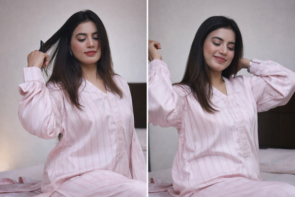 Woman in pink pajamas sitting on a bed, posing with her hair.