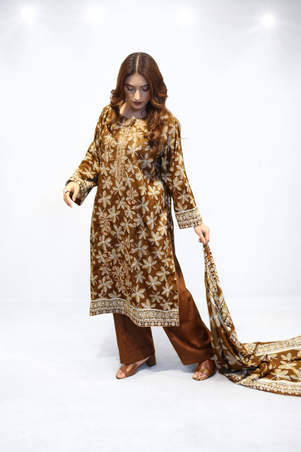 Woman wearing a brown and gold traditional outfit with a long scarf on a white background