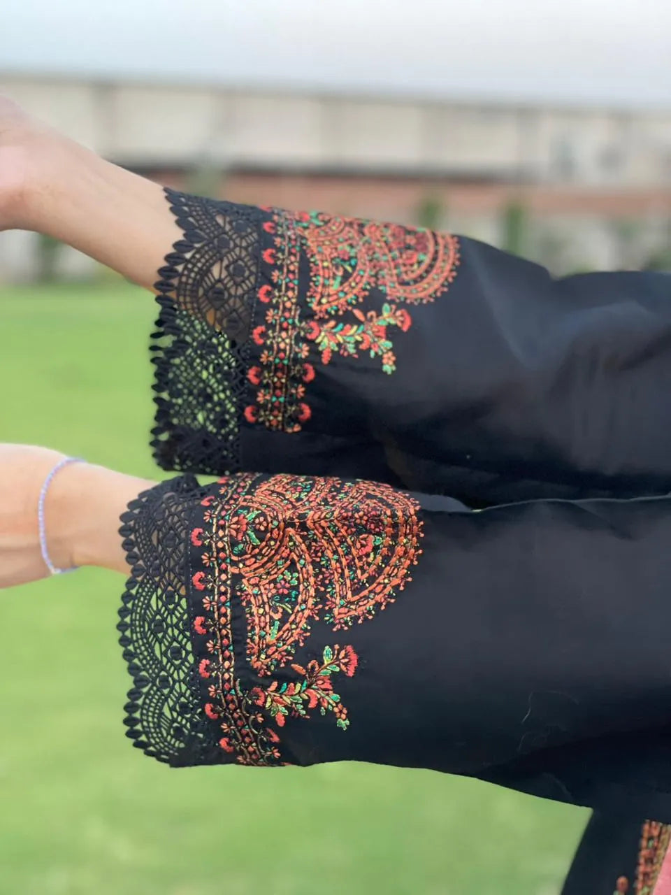 Black sleeve with intricate red and green embroidery against a blurred green background