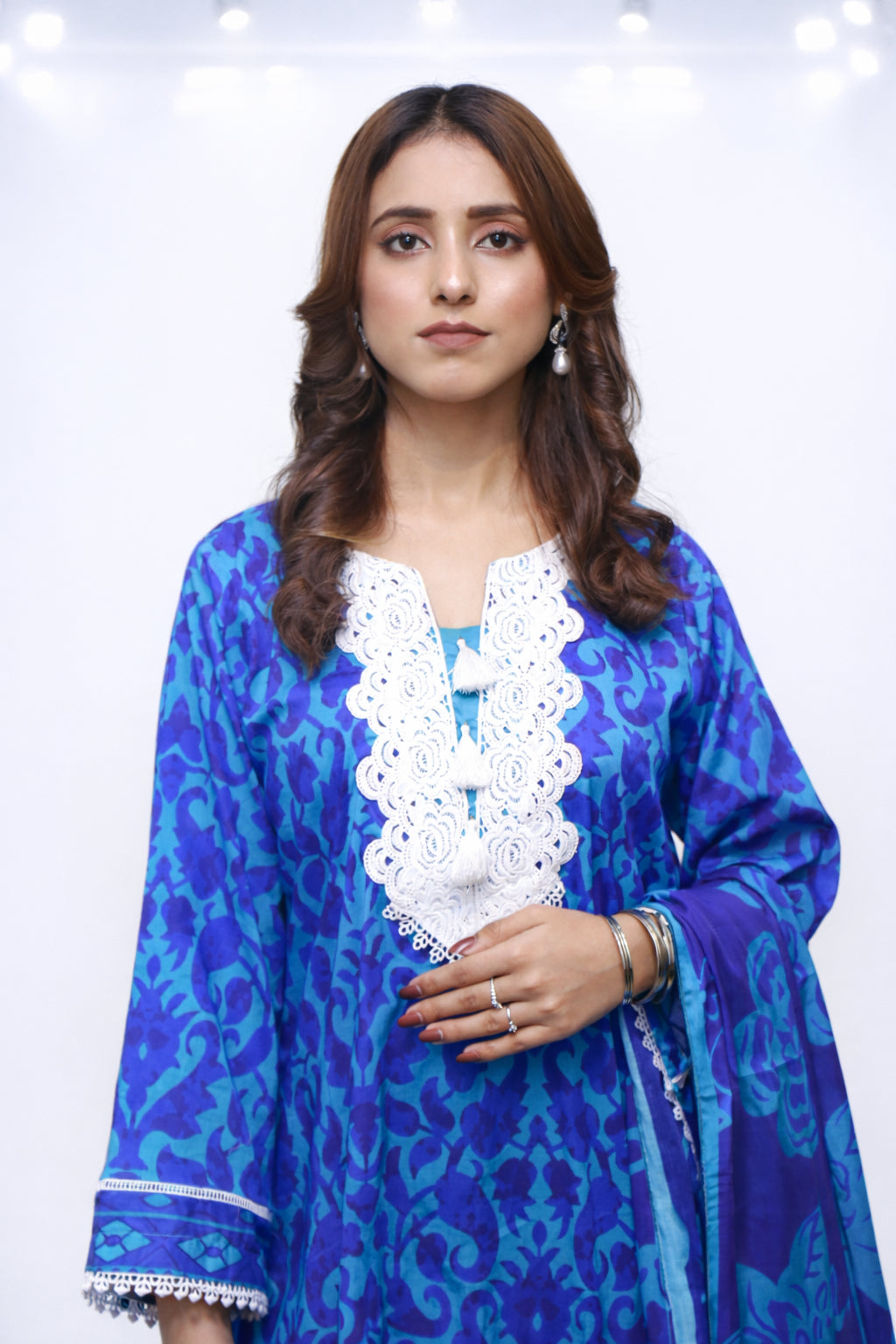Woman wearing a blue patterned dress with white lace details on a white background