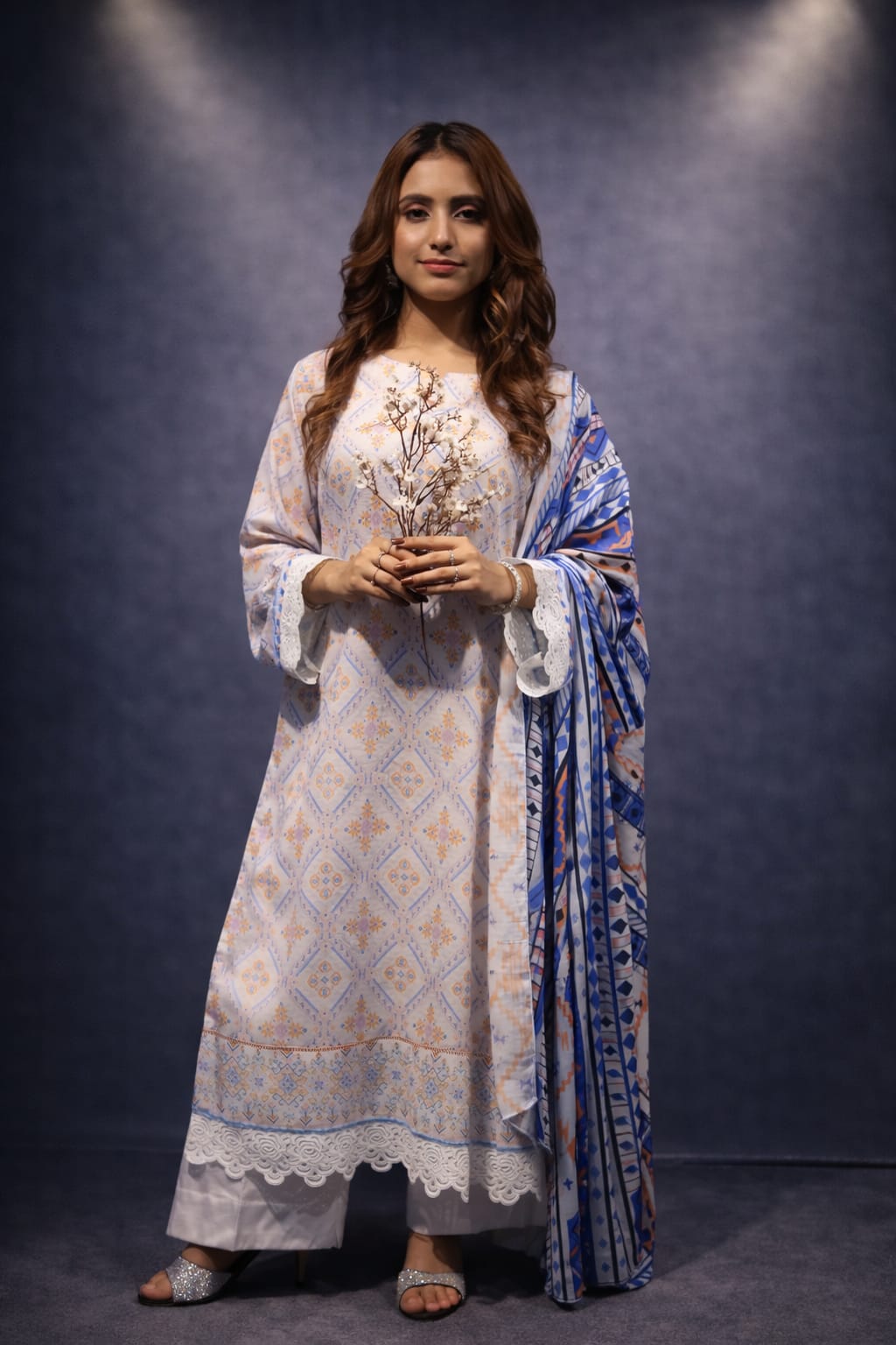 Woman in a traditional outfit with a blue and white patterned dupatta against a dark background