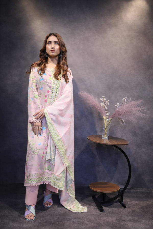 Woman in a light pink traditional outfit standing in front of a dark background with a small table and flowers.