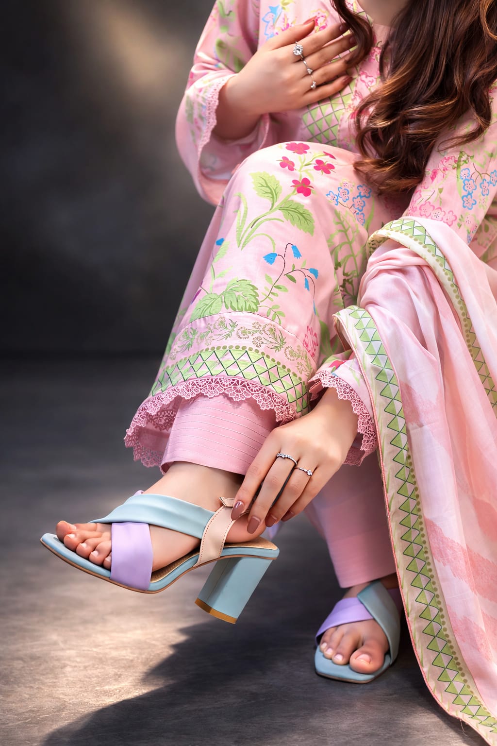Woman in a traditional outfit with floral patterns wearing light blue sandals on a dark background