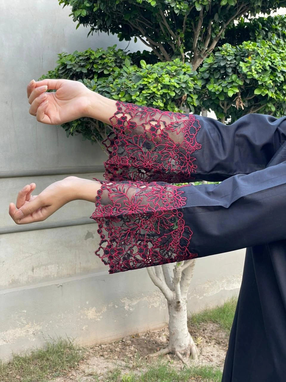 Person wearing a dark blue outfit with red lace sleeves against a green outdoor background