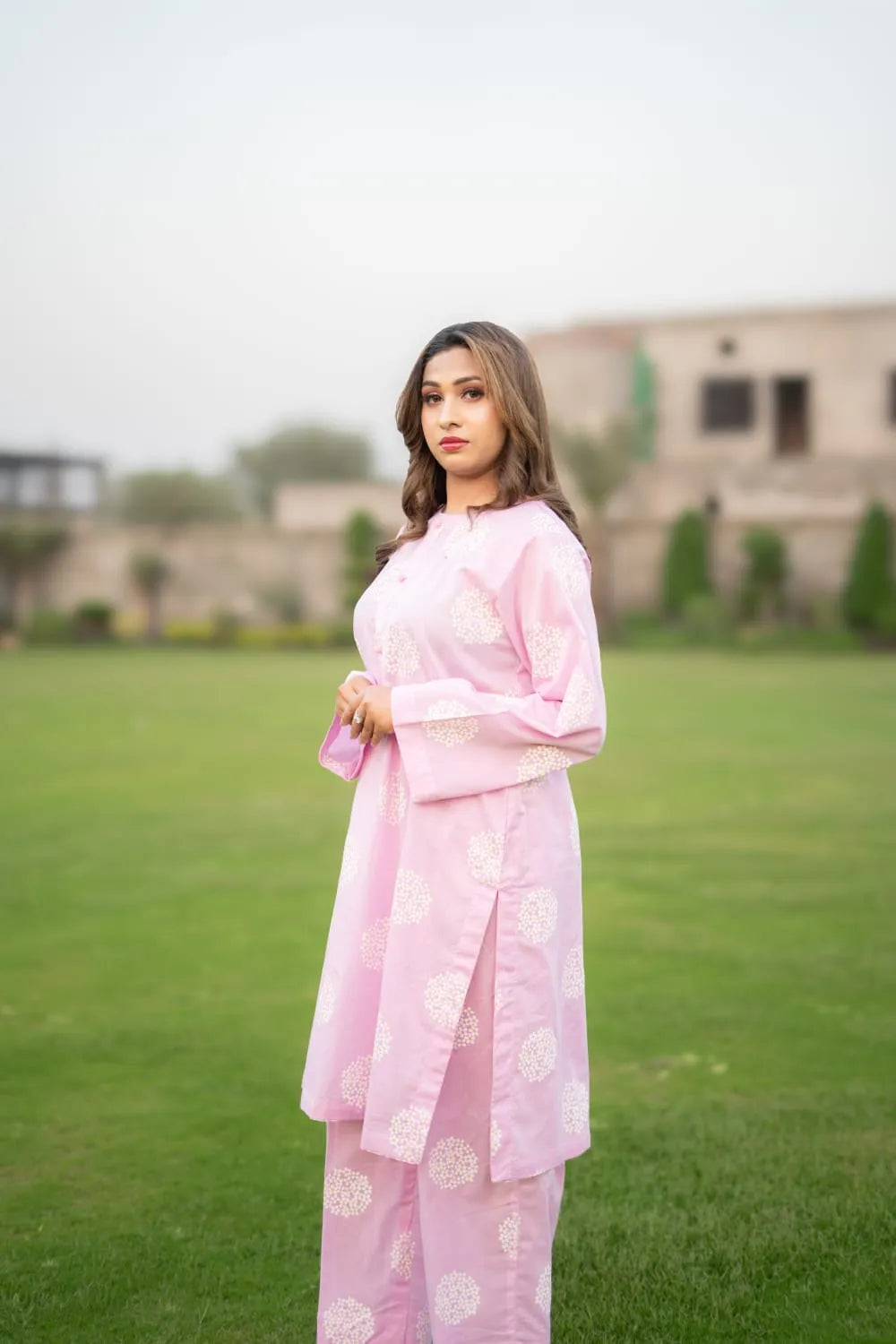 Woman in a pink traditional outfit standing on a grassy field with a blurred background