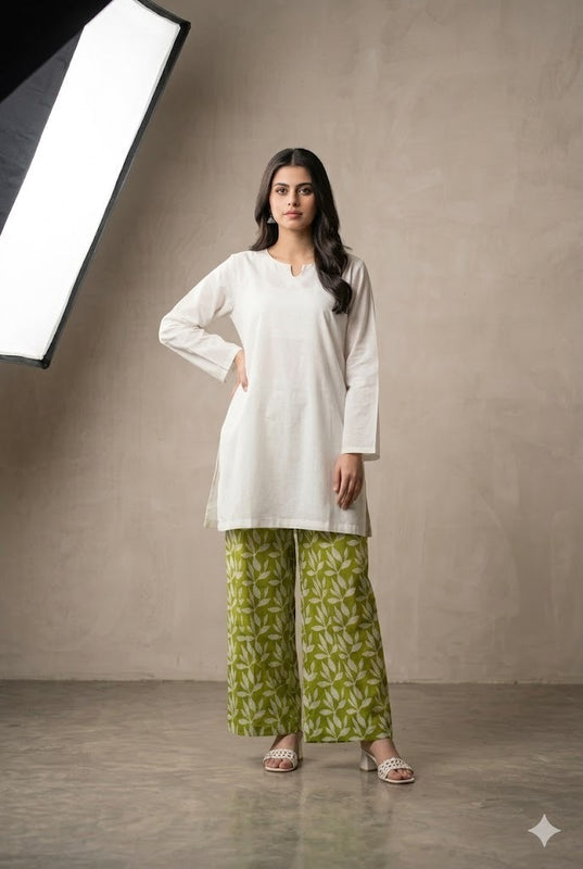 Woman wearing a white top and green patterned pants standing against a neutral background