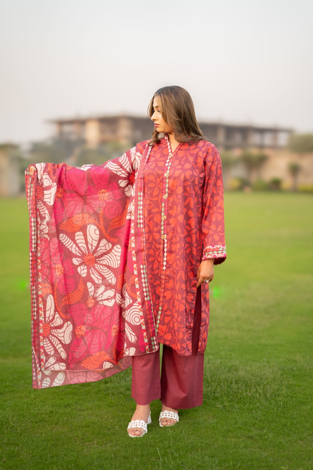Woman in a red traditional outfit with a floral dupatta standing on grass