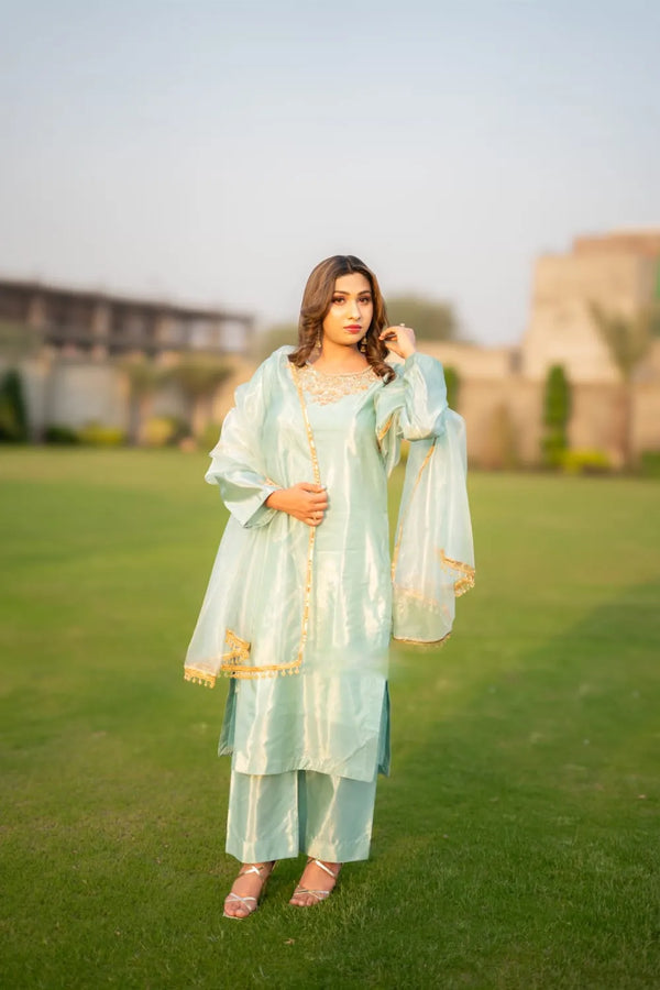 Woman in a light green traditional outfit standing on grass with a blurred background