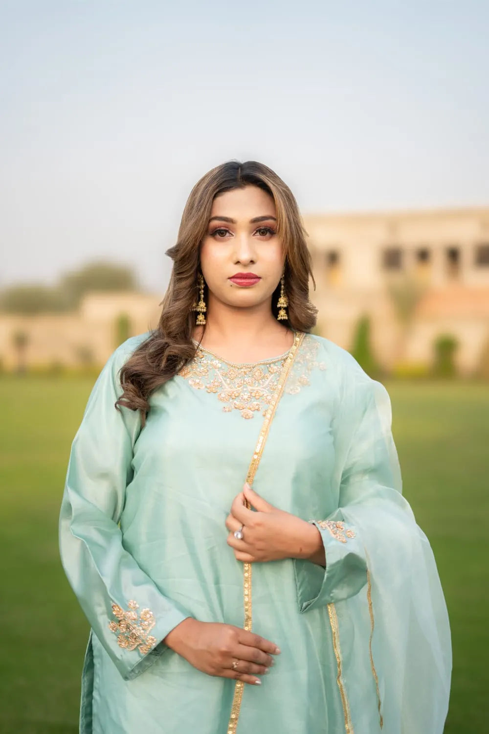 Woman in a light blue traditional outfit standing outdoors with a blurred background