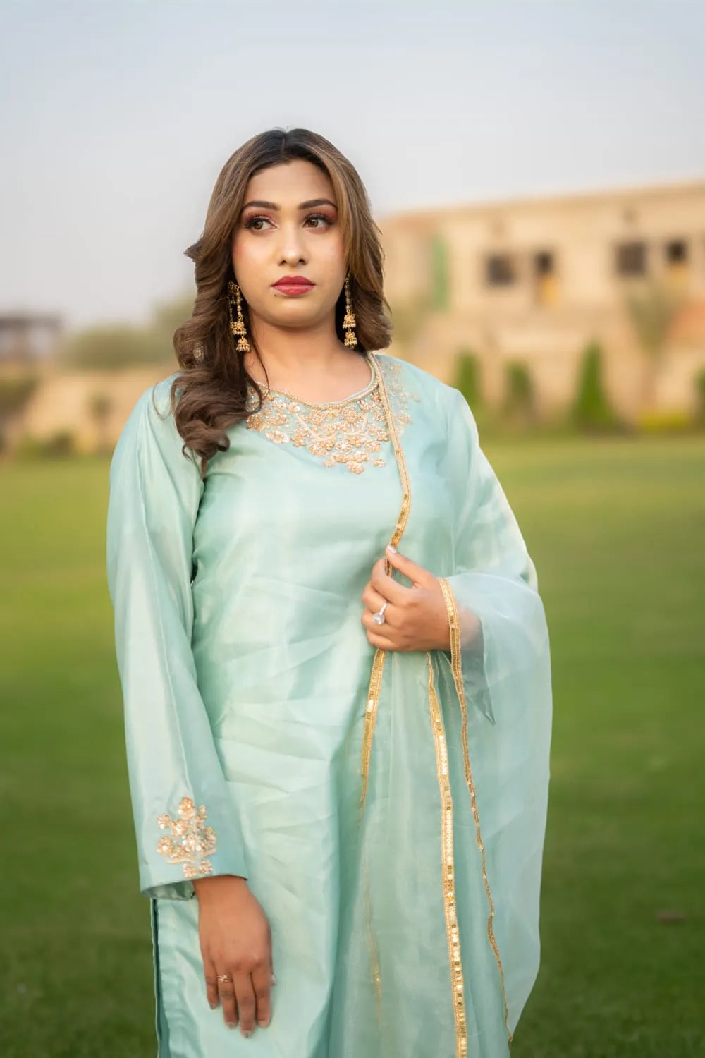 Woman in a light blue traditional outfit with gold details standing outdoors.