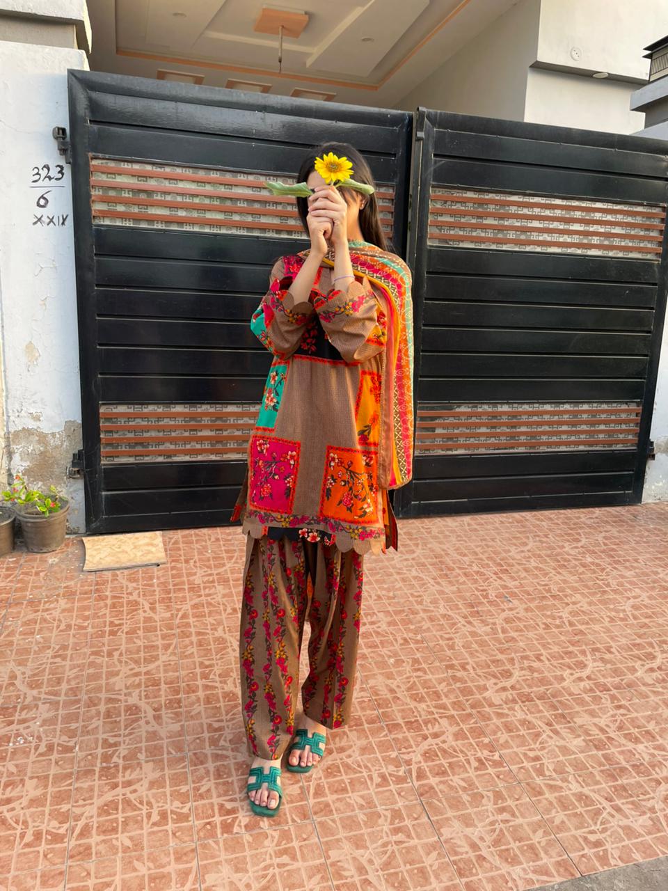 Person wearing a colorful traditional outfit standing in front of a gate.