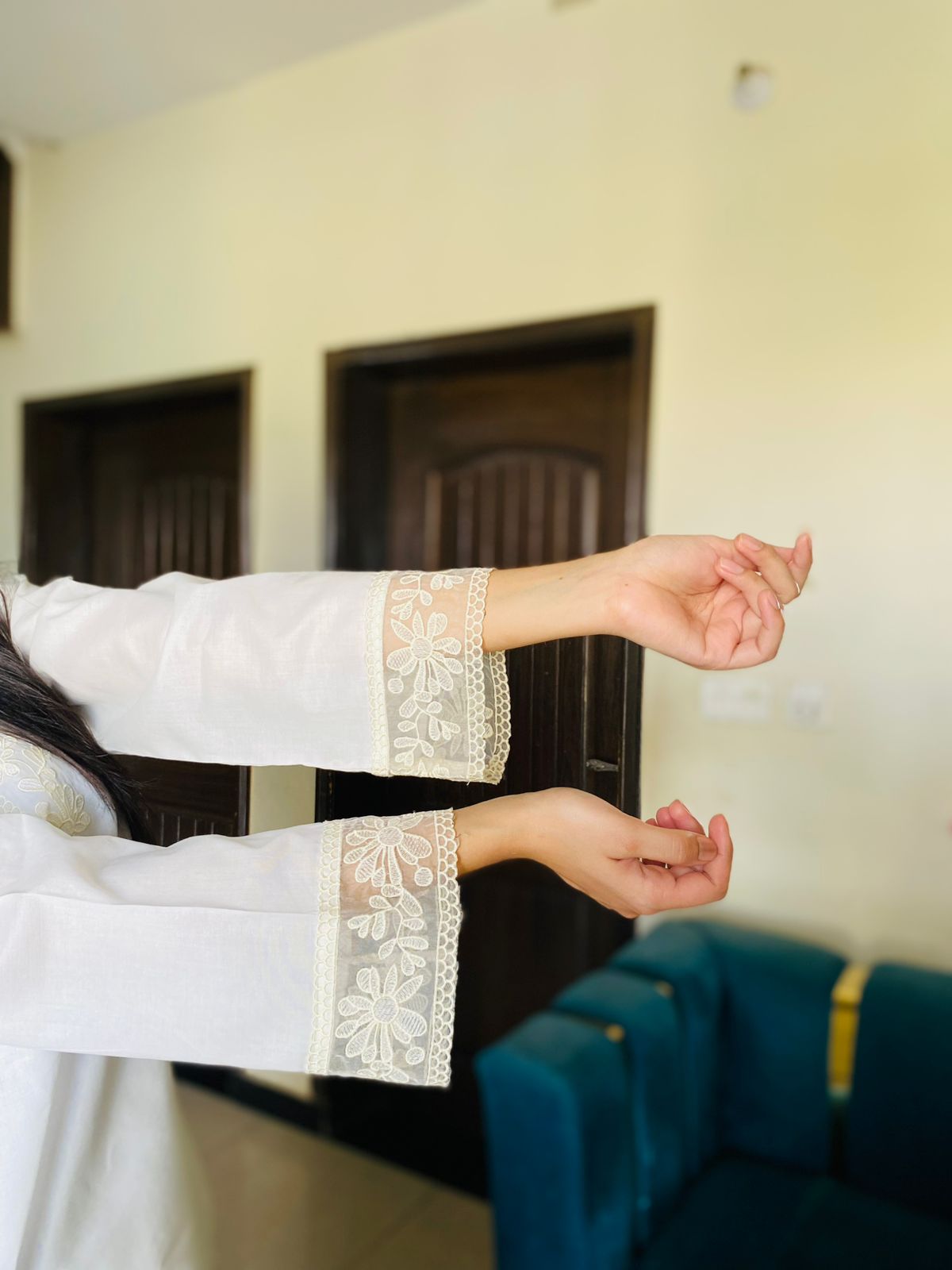 Person wearing a white outfit with lace cuffs in an indoor setting