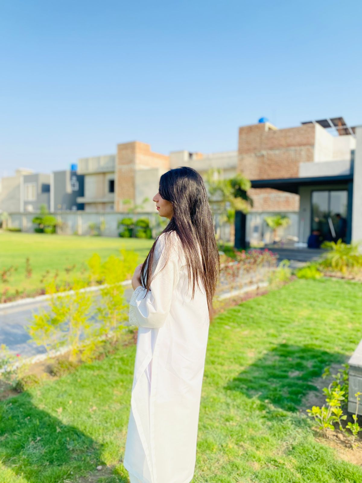 Woman in a white dress standing in a garden with modern buildings in the background
